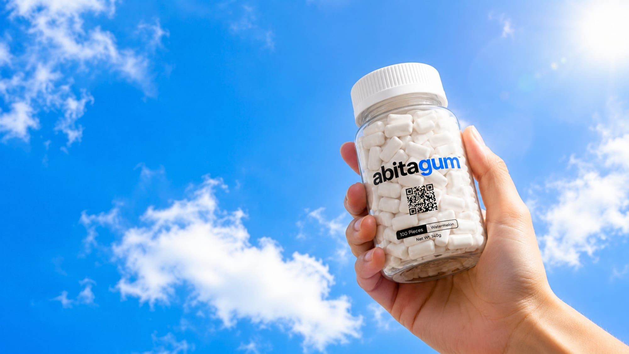 A hand holding a bottle of Abitagum focus gum against a blue sky